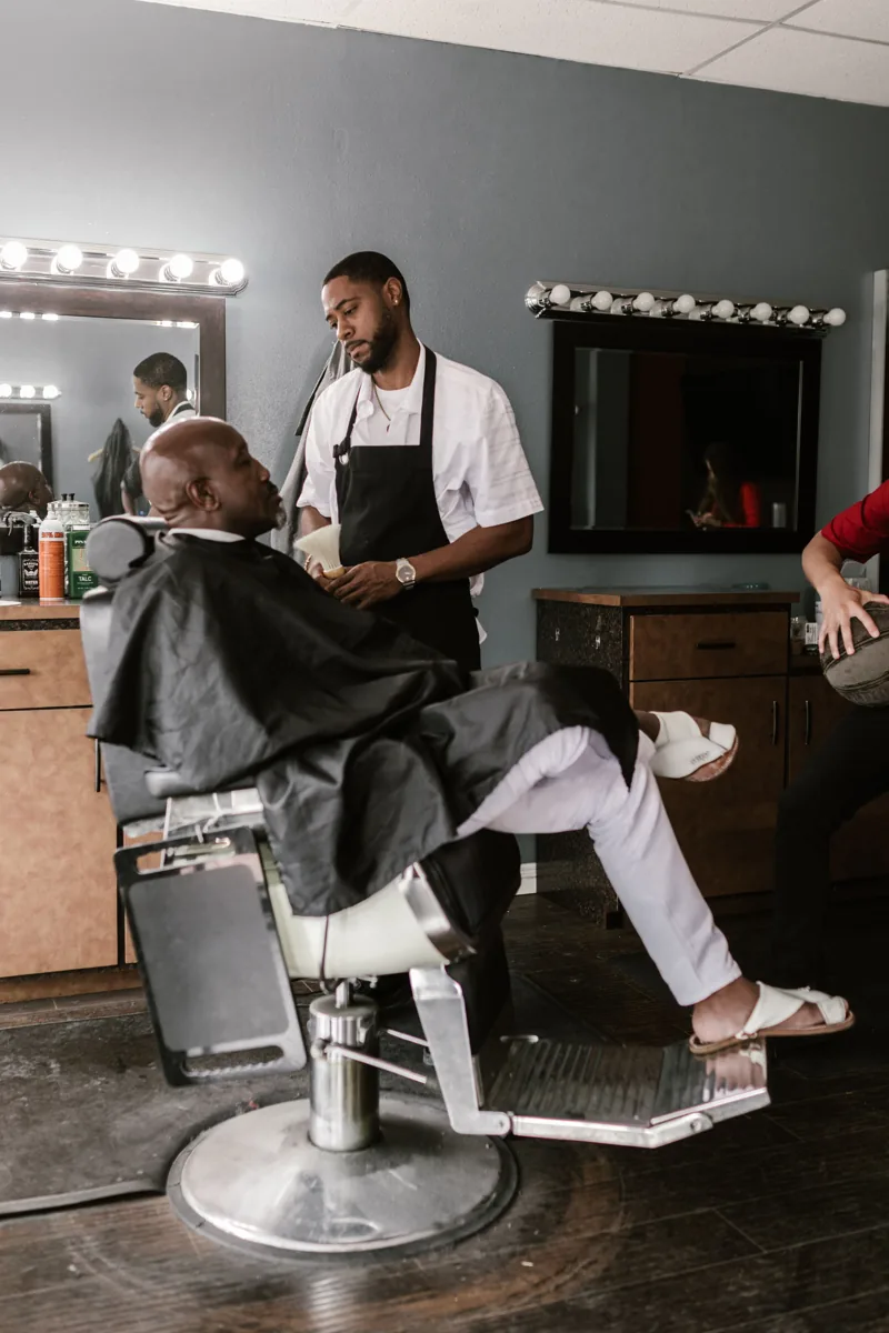 A barber working beside a seated client in a barbershop; stock concept photograph, not the SOULJA CUTS barber